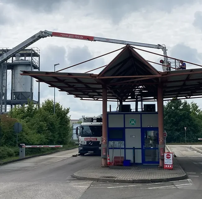 Hebebühne fährt über ein großes Einfahrt-Dach, Arbeiter säubern Dachkante nahe Industrieanlage.