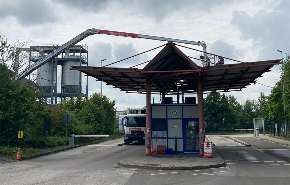 Hebebühne fährt über ein großes Einfahrt-Dach, Arbeiter säubern Dachkante nahe Industrieanlage.