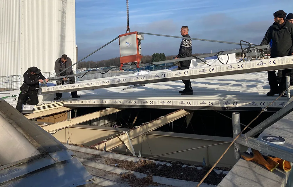 Montage von Sandwichpaneelen auf einem flach geneigten Industriedach mithilfe eines Krans.