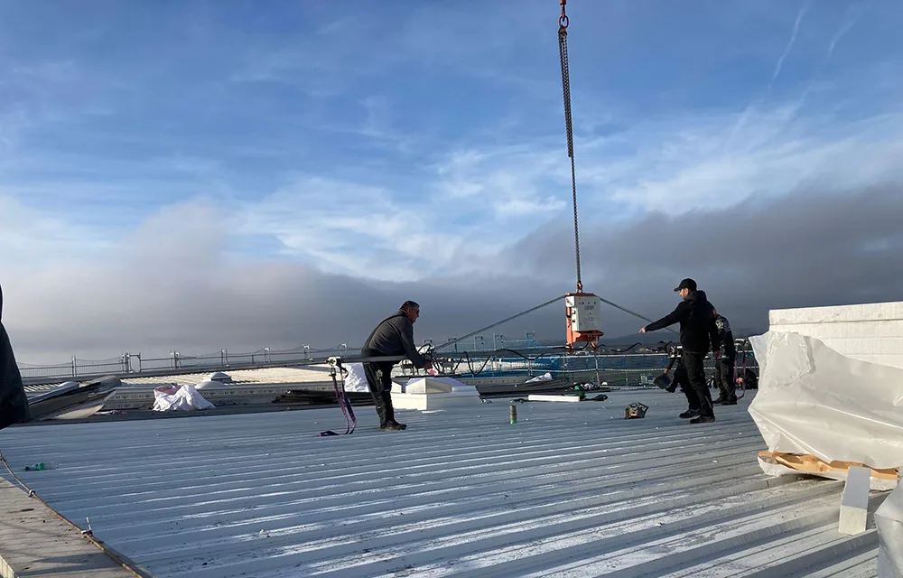 Dachdecker montieren Dachbauteile auf einem flach geneigten Metalldach mit Kranunterstützung.