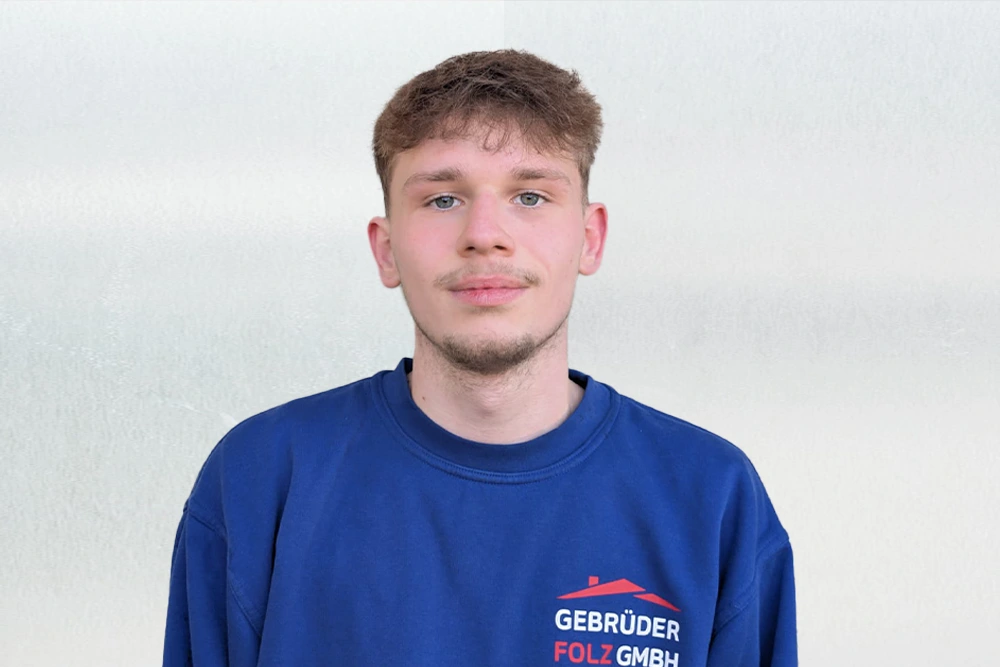 Portraitaufnahme von Leon mit blauem Pullover, lächelnd vor einem hellen Hintergrund.