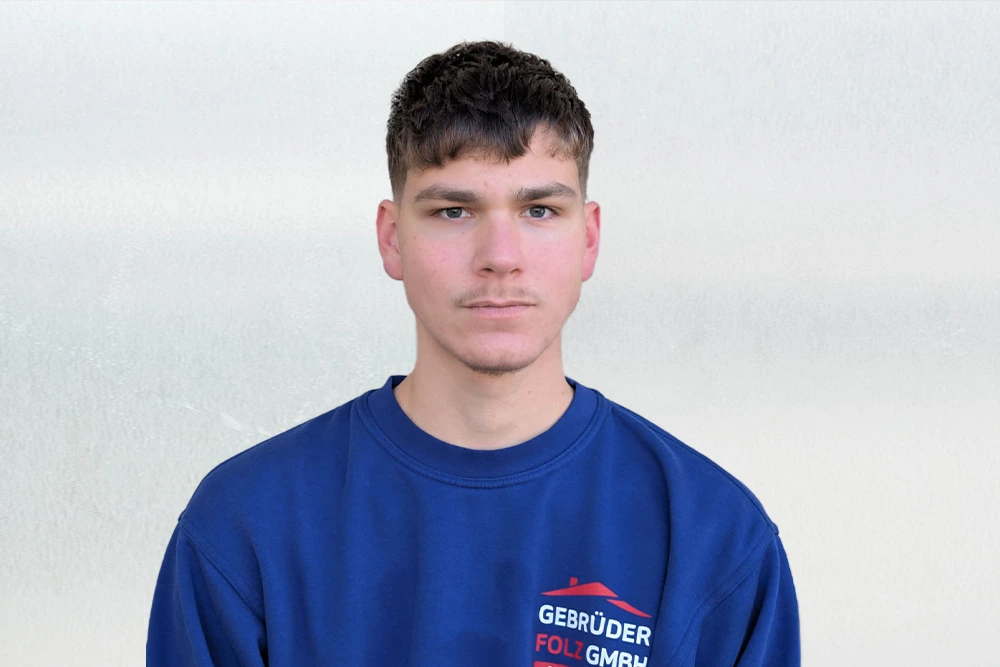 Portraitaufnahme von Lukas mit blauem Pullover vor einem hellen Hintergrund.