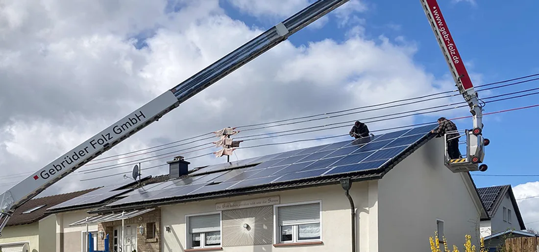 Zwei Arbeiter montieren Taubenschutz auf Dach, erreichbar über Hubarbeitsbühne neben Kran